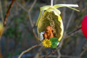 geöffnetes Osterei mit Stroh, Häschen und Blumen