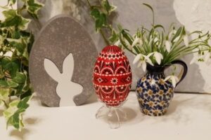 Osterwoche - rotes Osterei verziert mit weißem und schwarzem Wachs, Schneeglöckchen in einer Vase und Hasendekoration