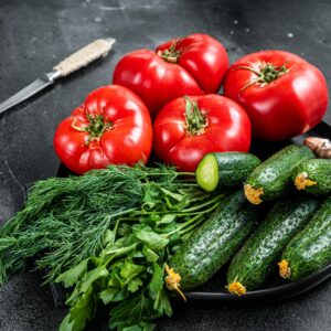 Tomaten, Gurken, Dill, Petersilie und Knoblauch auf einem dunklen Teller