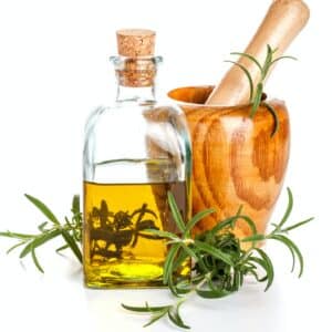 Rosmarinöl in einer Glasflasche mit Korken, daneben ein Holzmörser und frische Rosmarinzweige