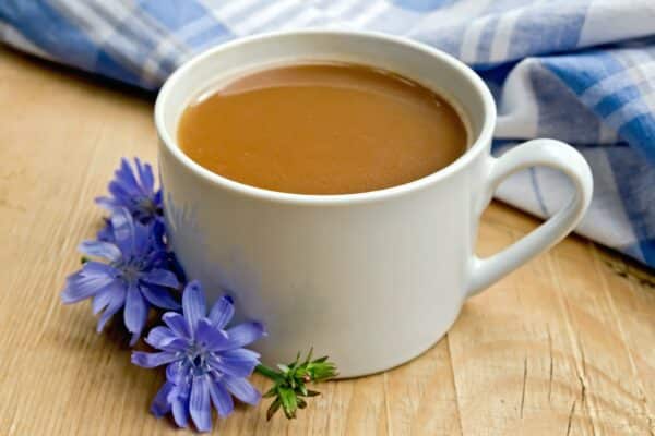Zichorienkaffee in einer weißen Tasse mit blauer Wegwartenblüte auf einem Holzbrett