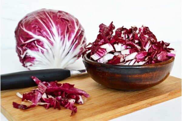 Radicchio-Kopf und geschnittene weinrote Blätter mit weißen Rippen in einer Holzschale