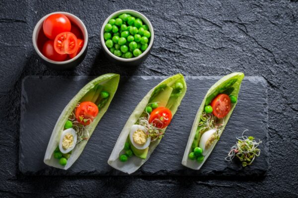 Chicorée-Blätter gefüllt mit Salat aus Ei, Sprossen und Avocado auf einem Teller