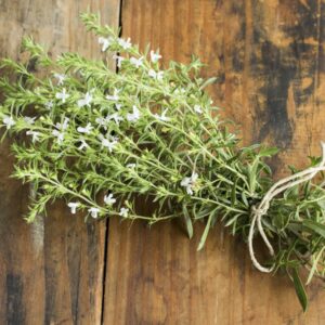 Gebundener Strauß blühendes Bohnenkraut mit weißen Blüten auf einem Holzbrett