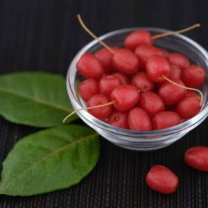 Rote Ölweidenfrüchte in einer Glasschale neben zwei grünen Blättern