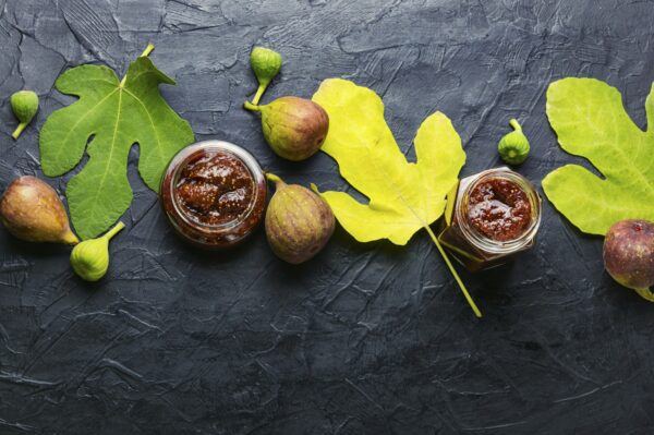 Zwei Gläser hausgemachtes Feigen-Chutney zwischen frischen Feigen und Feigenblättern