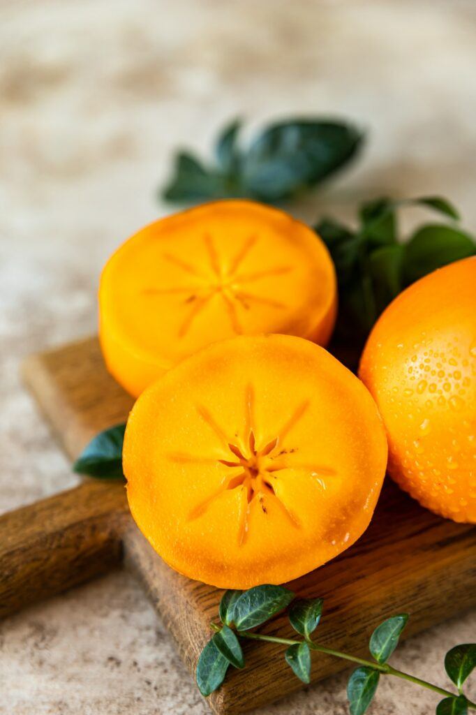 Ganze und halbierte reife orange Kakifrüchte auf einem hölzernen Schneidebrett