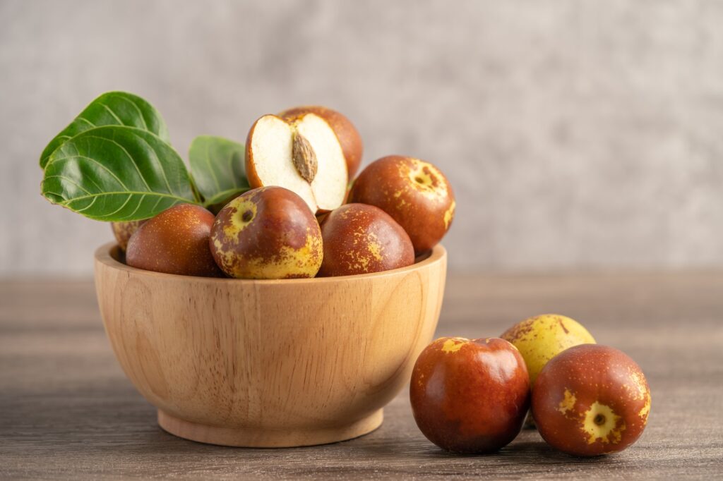 Frische Jujube-Früchte in einer Holzschale, eine davon aufgeschnitten mit hellem Fruchtfleisch und Kern