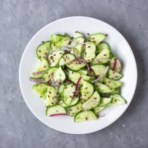 Gurkensalat mit Leinsamen und roten Zwiebeln auf einem weißen Teller