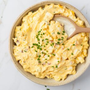 Eiersalat mit Schnittlauch in einer Keramikschüssel mit Holzlöffel, von oben auf weißem Marmor
