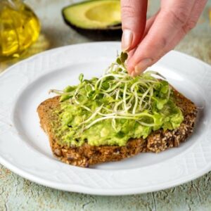 Frau gibt Microgreens auf leckeres Toast