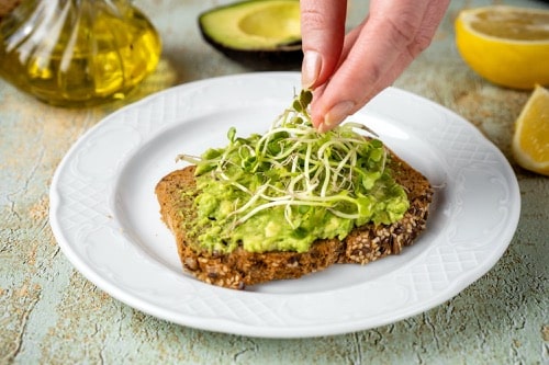 Frau gibt Microgreens auf leckeres Toast