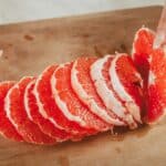 Geschälte Grapefruitscheiben werden von Hand auf einem Holzbrett angerichtet.