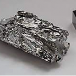 Rohes Schungit-Mineral neben Würfel zur Größenvergleich auf weißem Hintergrund.