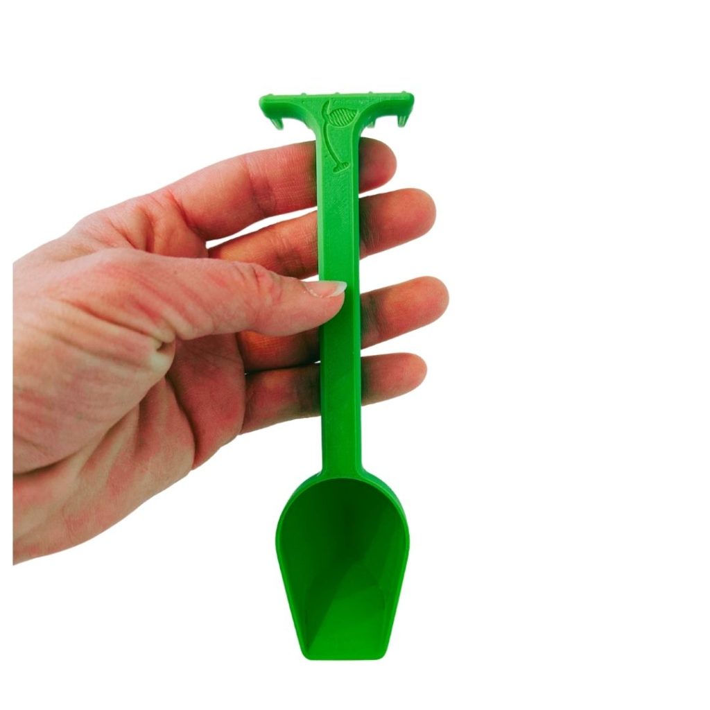 Kleine grüne Dosierungsschaufel für präzise Portionierung von organischem Dünger in der Hand